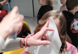 fryzjerka osłaniając twarz dziecka nadaje kolor włosom sprayem